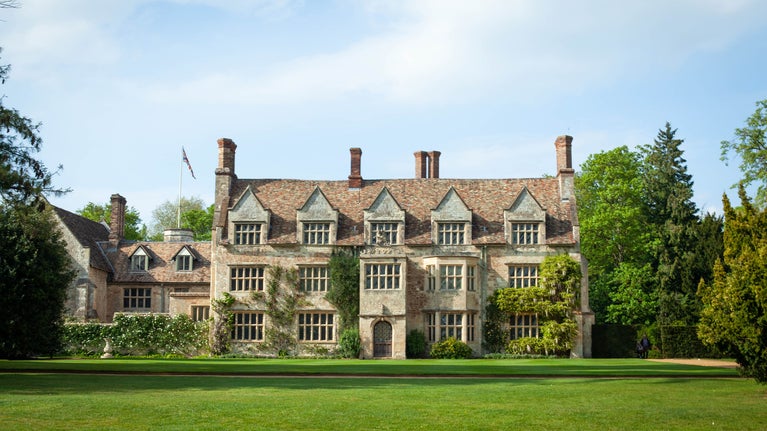 An early summer photo showing a stone Jacobean house with blue sky and green trees